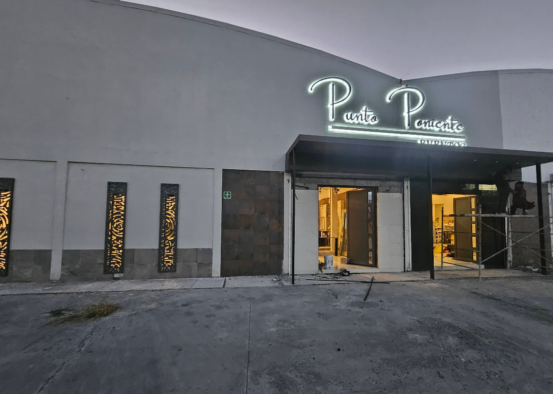 Fachada de Punto Poniente Eventos de noche con letrero de neón